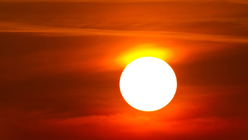 A brightly glowing sun is centered in a scene of orange and red clouds.