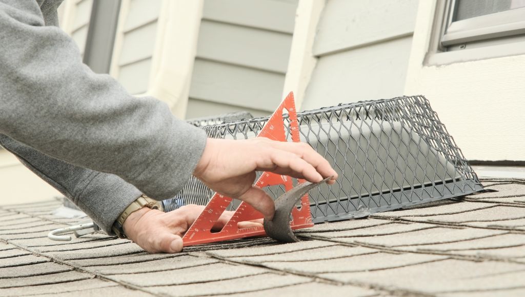 A professional roofer tests the flexibility of an asphalt shingle on a residential roof using a rafter square to determine how much flexibility remains.