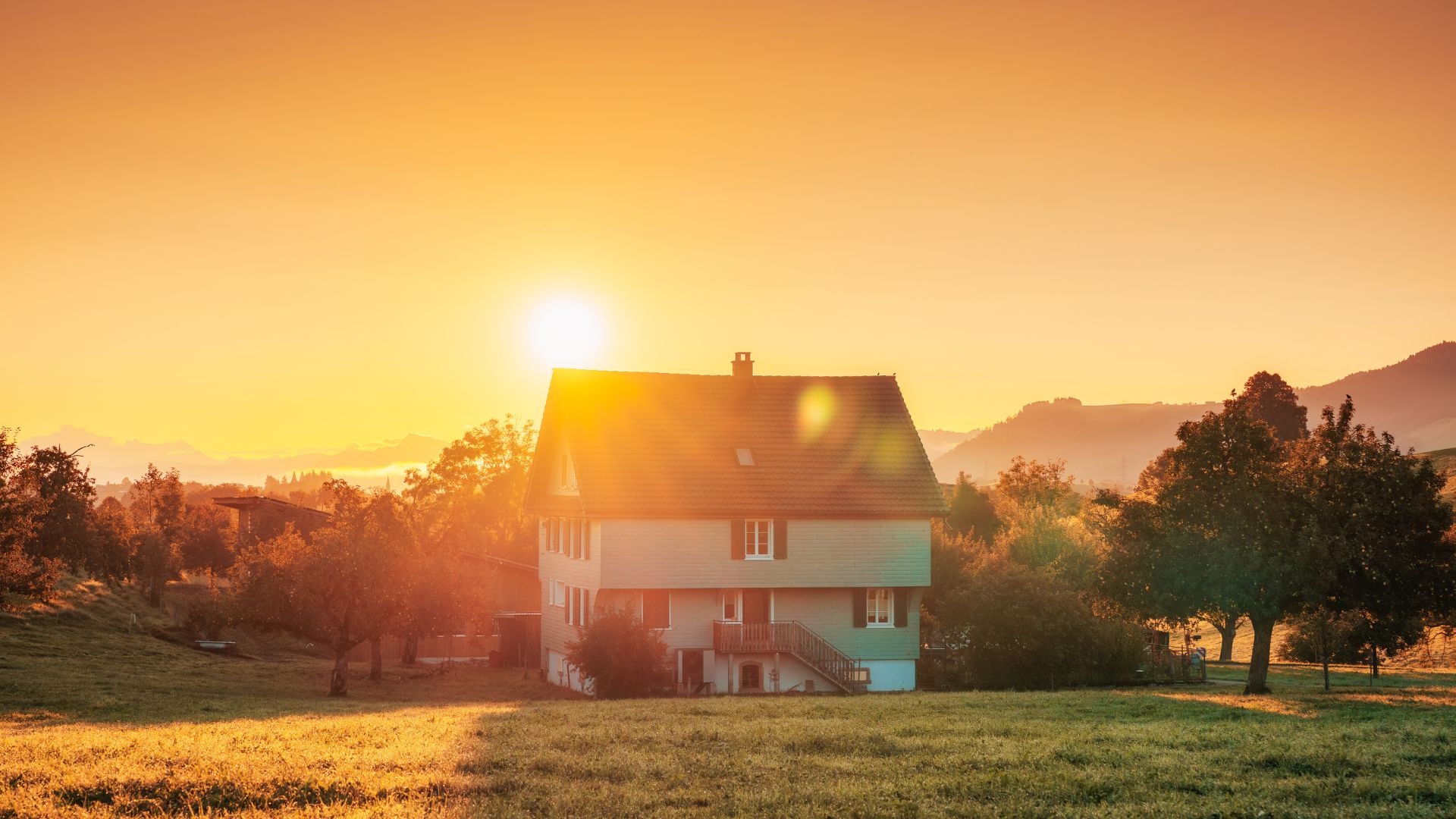UV Rays NORR Hero The sun rises over a rural house surrounded by trees. The UV rays shine directly onto the asphalt shingles.
