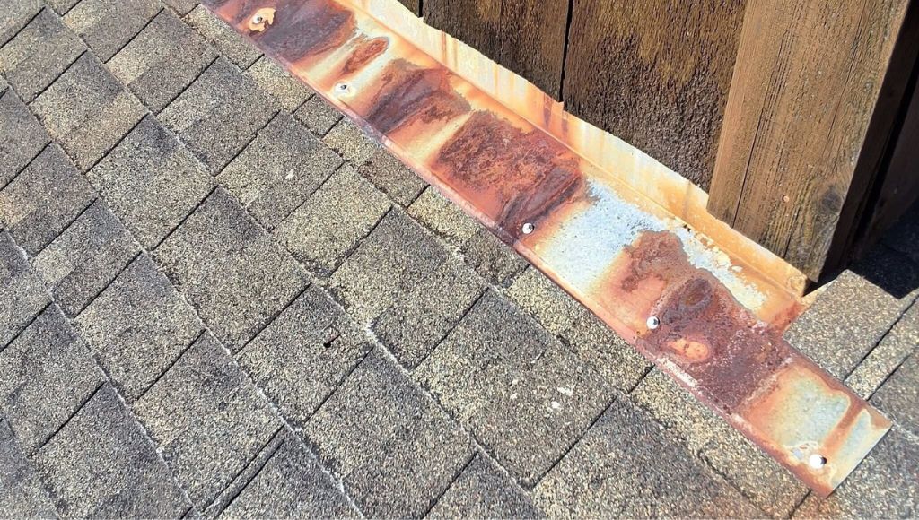 Closeup of sun-damaged shingles and exposed, rusted, and damaged flashing.